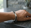 Person wearing a silver and black beaded bracelet on a dark surface