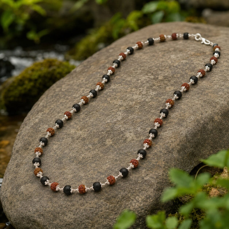 Necklace with black, red, and silver beads on a rock with a natural background