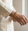 Gold bracelet with red stones on a wrist, wearing a beige outfit.